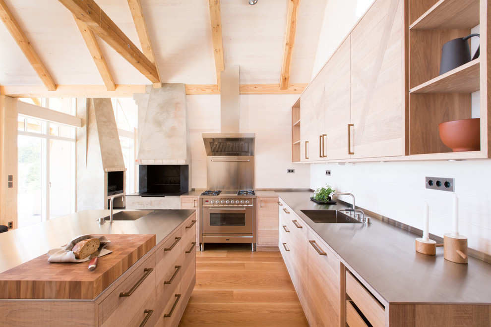 Foto på ett stort skandinaviskt l-kök, med släta luckor, skåp i ljust trä, rostfria vitvaror, mellanmörkt trägolv, en köksö, en enkel diskho, träbänkskiva och stänkskydd med metallisk yta