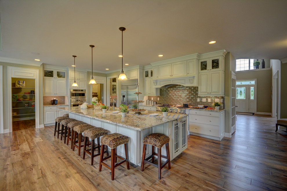 Huge transitional l-shaped light wood floor open concept kitchen photo in Philadelphia with an undermount sink, glass-front cabinets, distressed cabinets, granite countertops, beige backsplash, glass tile backsplash, stainless steel appliances and two islands