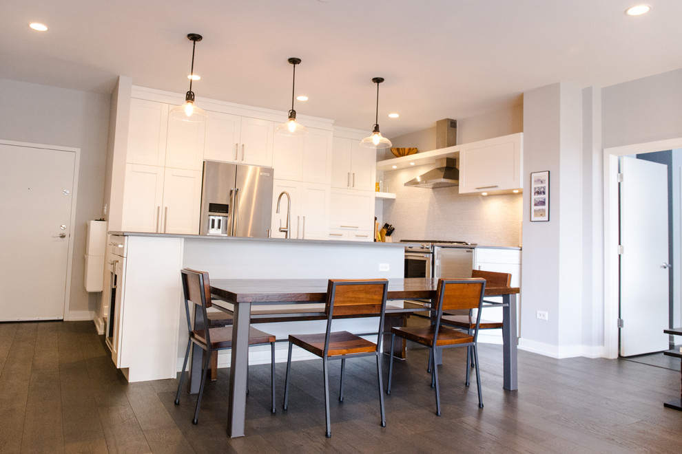 Photo of a medium sized contemporary l-shaped open plan kitchen in Chicago with a submerged sink, recessed-panel cabinets, white cabinets, engineered stone countertops, grey splashback, stone tiled splashback, stainless steel appliances, dark hardwood flooring and an island.