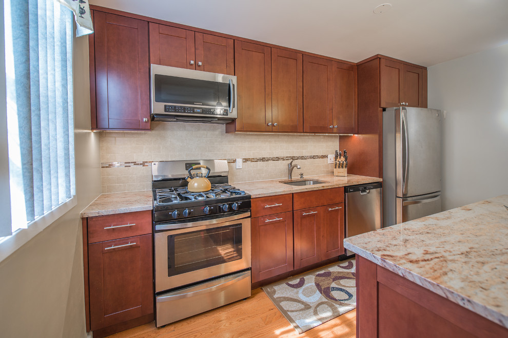 Mid-sized transitional single-wall medium tone wood floor eat-in kitchen photo in New York with an undermount sink, shaker cabinets, medium tone wood cabinets, granite countertops, brown backsplash, stainless steel appliances, an island and stone tile backsplash