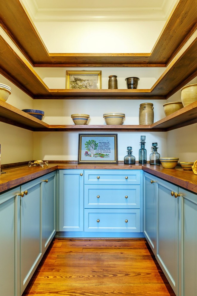 Country Küche in U-Form mit Vorratsschrank, Schrankfronten im Shaker-Stil, blauen Schränken, Arbeitsplatte aus Holz, dunklem Holzboden, braunem Boden und brauner Arbeitsplatte in Sonstige