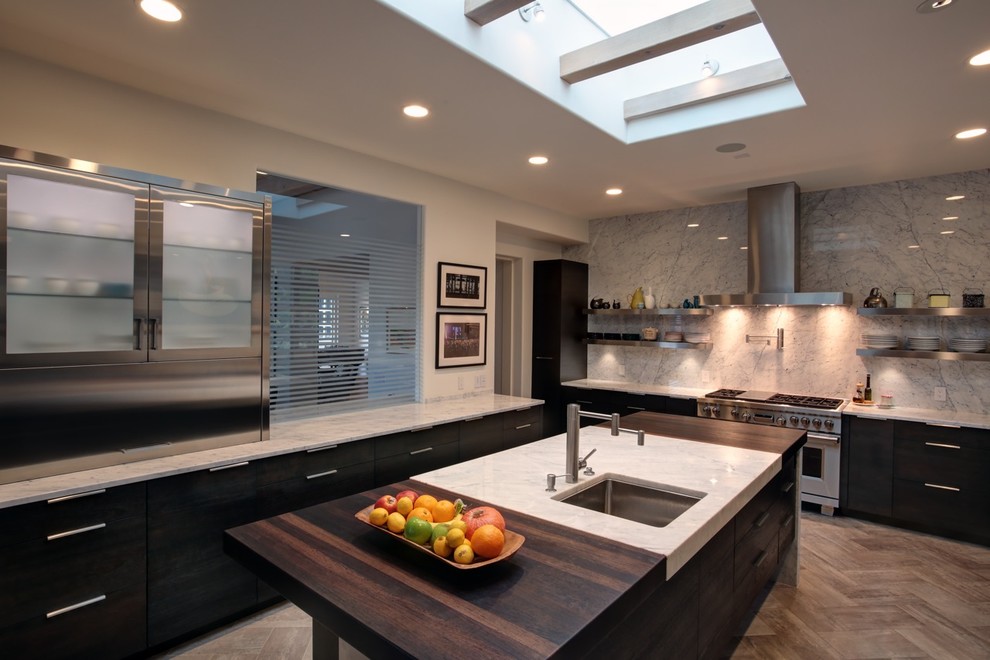 Design ideas for a large contemporary galley kitchen/diner in Santa Barbara with a belfast sink, flat-panel cabinets, dark wood cabinets, engineered stone countertops, white splashback, porcelain splashback, stainless steel appliances, painted wood flooring and an island.