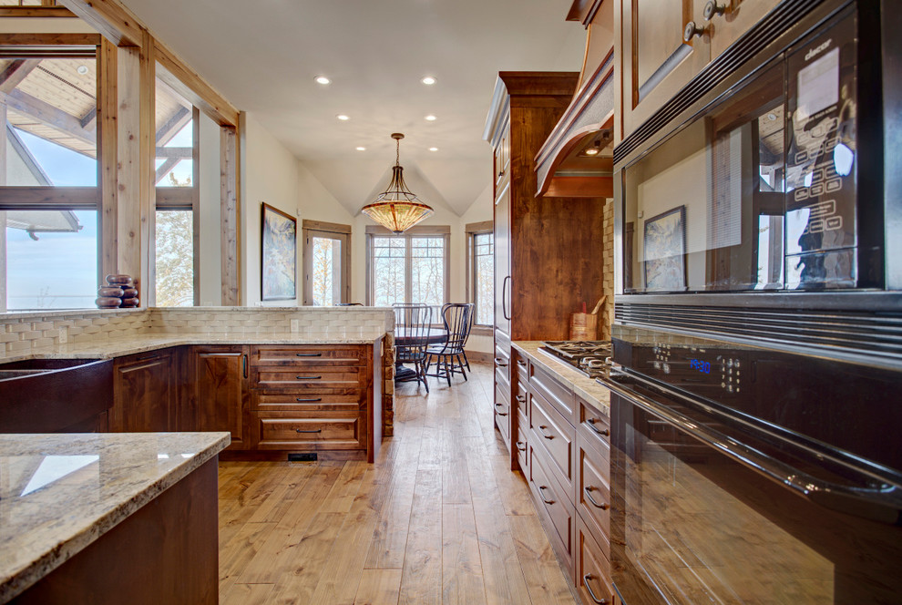 Example of a mid-sized mountain style u-shaped medium tone wood floor and brown floor eat-in kitchen design in Calgary with a farmhouse sink, raised-panel cabinets, medium tone wood cabinets, granite countertops, white backsplash, ceramic backsplash, paneled appliances and a peninsula