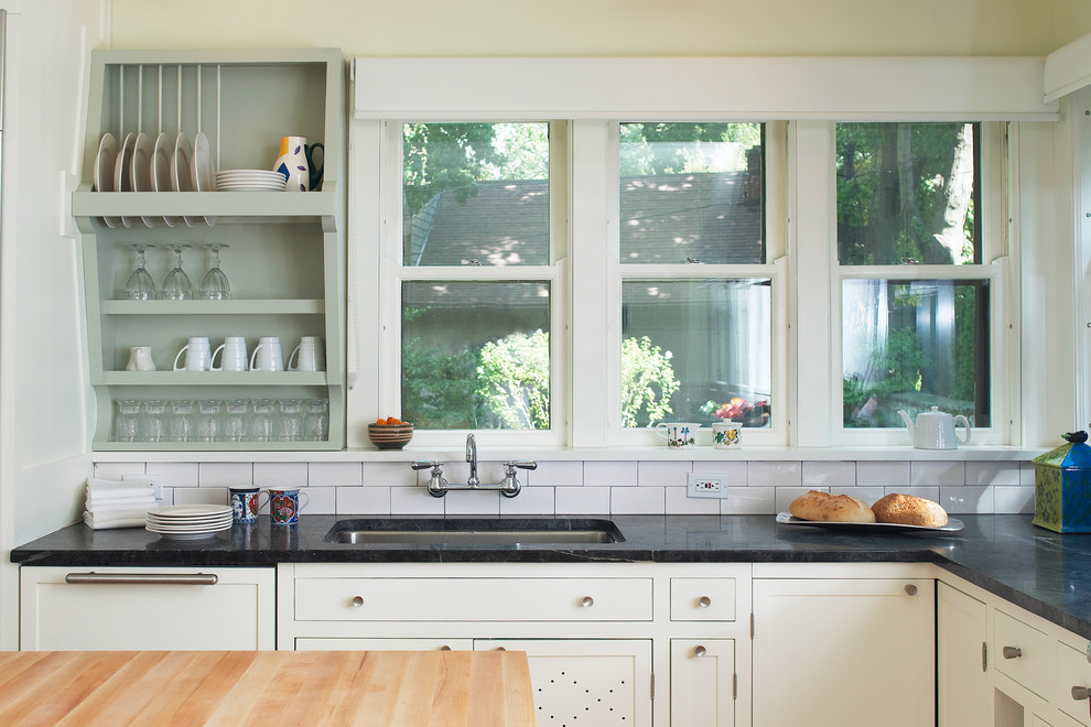Klassisk inredning av ett avskilt, mellanstort l-kök, med en undermonterad diskho, luckor med infälld panel, vita skåp, bänkskiva i täljsten, vitt stänkskydd, stänkskydd i keramik, integrerade vitvaror, ljust trägolv och en köksö