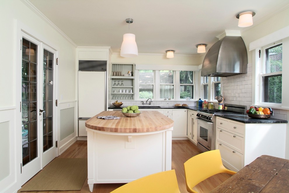 Eat-in kitchen - mid-sized transitional l-shaped light wood floor eat-in kitchen idea in New York with soapstone countertops, recessed-panel cabinets, white cabinets, white backsplash, subway tile backsplash, white appliances, an undermount sink and an island