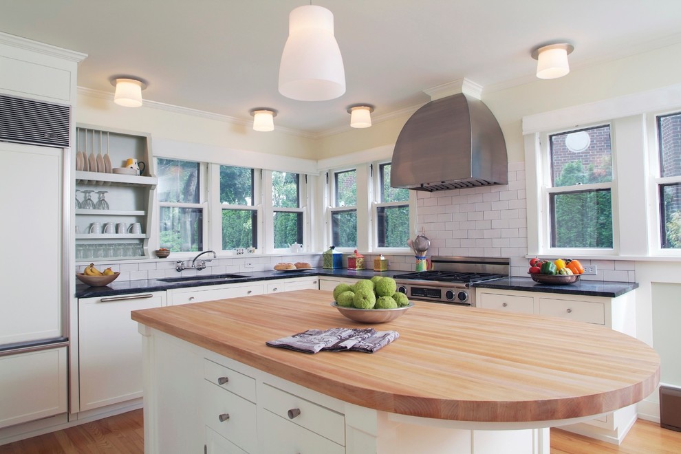 Photo of a medium sized traditional l-shaped kitchen/diner in New York with a submerged sink, recessed-panel cabinets, white cabinets, soapstone worktops, white splashback, ceramic splashback, integrated appliances, light hardwood flooring and an island.