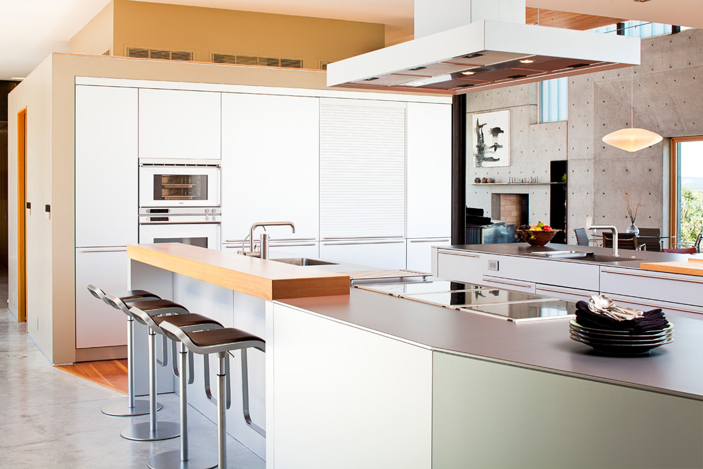 Bild på ett stort funkis linjärt kök, med en undermonterad diskho, släta luckor, rostfria vitvaror, betonggolv och flera köksöar