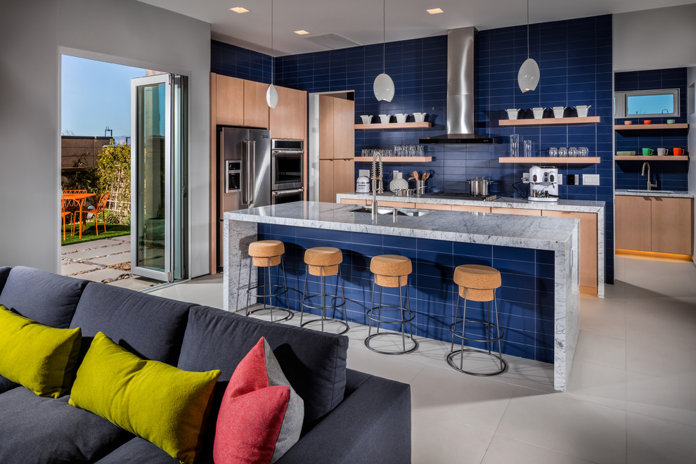 Diseño de cocinas en L contemporánea con fregadero bajoencimera, armarios con paneles lisos, puertas de armario de madera clara, salpicadero azul, electrodomésticos de acero inoxidable y una isla