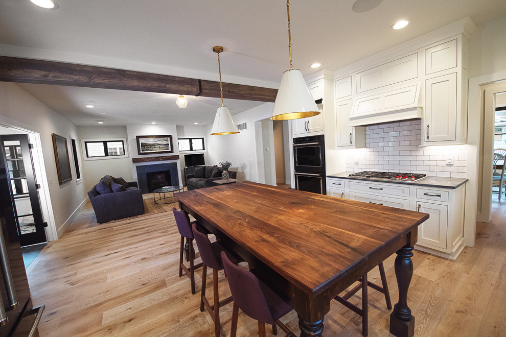 Inspiration for a large transitional u-shaped medium tone wood floor kitchen remodel in Other with a farmhouse sink, shaker cabinets, white cabinets, solid surface countertops, white backsplash, subway tile backsplash, stainless steel appliances and an island