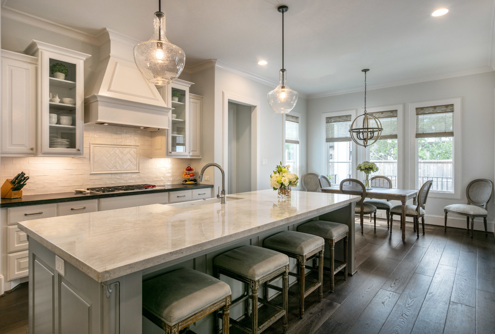 Imagen de cocina lineal, clásica, grande, abierta, con fregadero sobremueble, puertas de armario blancas, salpicadero blanco, salpicadero de azulejos tipo metro, electrodomésticos de acero inoxidable, suelo de madera en tonos medios, una isla, suelo marrón y encimeras grises