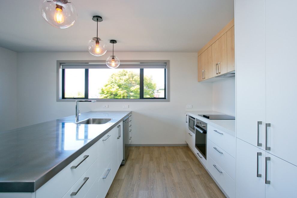 Moderne Küche mit weißen Schränken, Edelstahl-Arbeitsplatte, Küchenrückwand in Weiß, Glasrückwand, Küchengeräten aus Edelstahl und Laminat in Dunedin