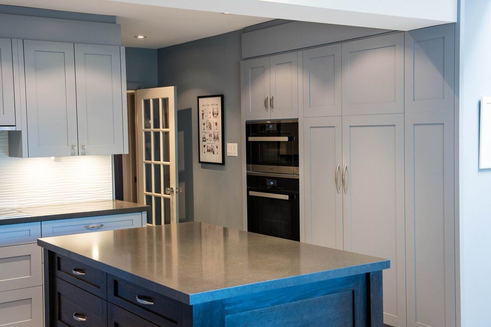 Photo of a medium sized contemporary l-shaped open plan kitchen in Toronto with a double-bowl sink, shaker cabinets, blue cabinets, white splashback, stone slab splashback, stainless steel appliances, light hardwood flooring and an island.