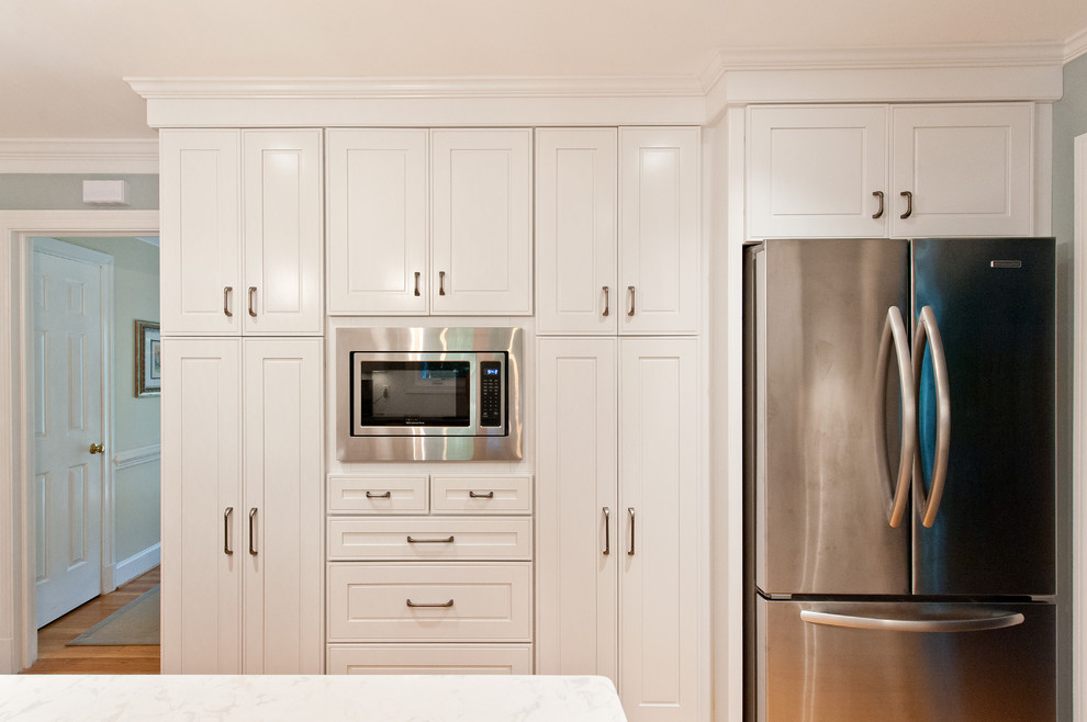 Foto di una cucina minimalista di medie dimensioni con ante con bugna sagomata, ante bianche, elettrodomestici in acciaio inossidabile e parquet chiaro
