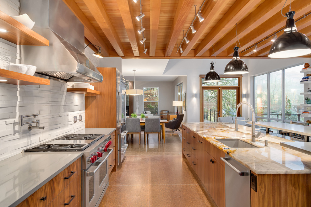 Bild på ett stort funkis kök, med en undermonterad diskho, släta luckor, skåp i mellenmörkt trä, granitbänkskiva, stänkskydd i stenkakel, rostfria vitvaror, betonggolv, en köksö, vitt stänkskydd och brunt golv