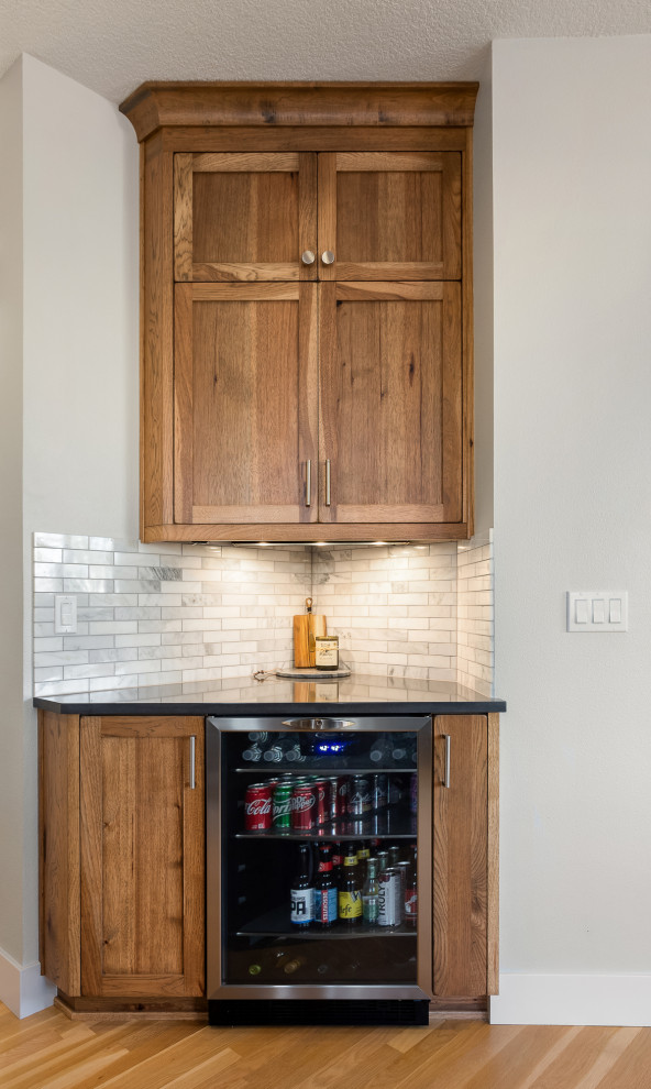 Mid-sized mountain style l-shaped light wood floor and brown floor home bar photo in Portland with an undermount sink, shaker cabinets, medium tone wood cabinets, granite countertops, white backsplash, marble backsplash and gray countertops