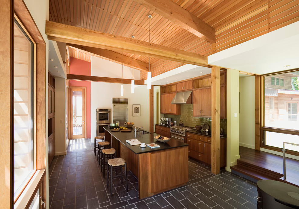 Bild på ett mellanstort 50 tals kök, med en enkel diskho, släta luckor, skåp i mellenmörkt trä, granitbänkskiva, beige stänkskydd, stänkskydd i tunnelbanekakel, rostfria vitvaror, skiffergolv och en köksö