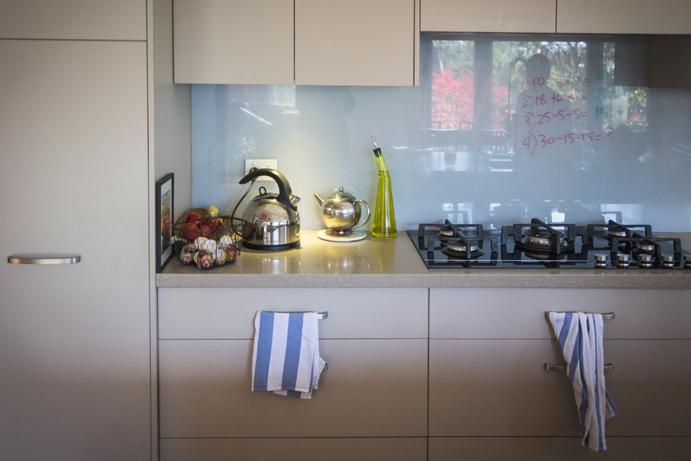 Medium sized traditional galley open plan kitchen in Sydney with a double-bowl sink, flat-panel cabinets, beige cabinets, engineered stone countertops, glass sheet splashback, stainless steel appliances, medium hardwood flooring and an island.