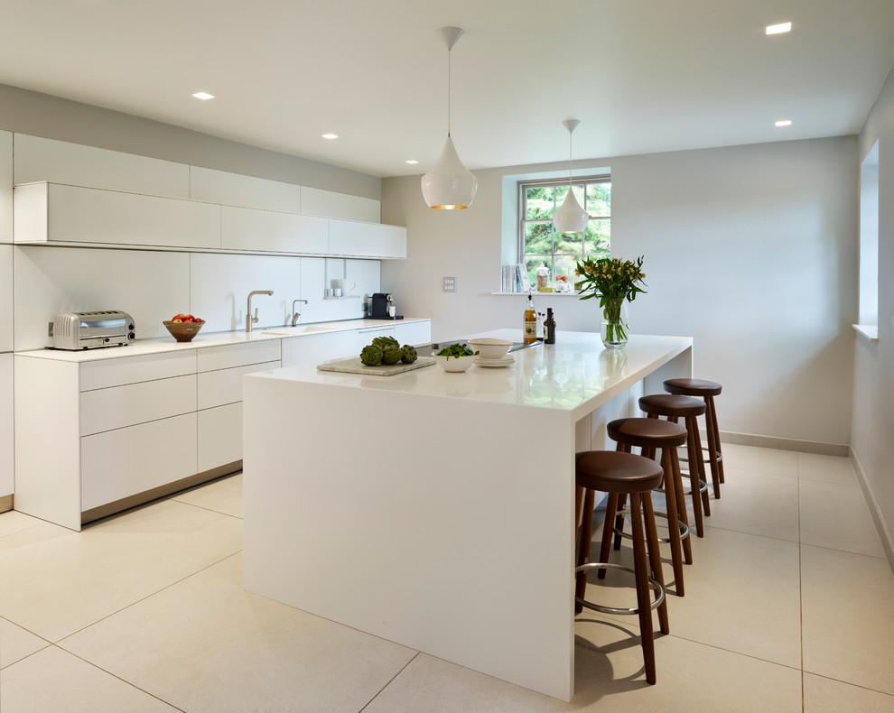 Moderne Wohnküche mit integriertem Waschbecken, flächenbündigen Schrankfronten, weißen Schränken, Küchenrückwand in Weiß, Glasrückwand, Porzellan-Bodenfliesen und Kücheninsel in Wiltshire