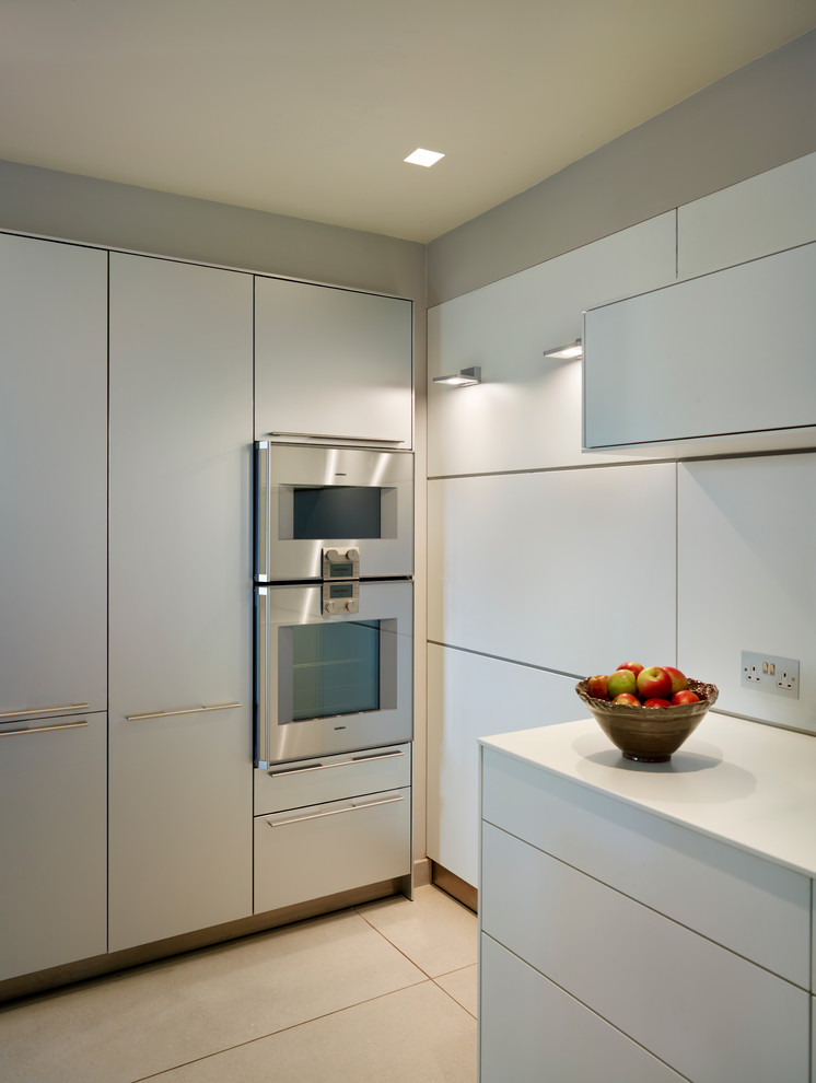 Moderne Wohnküche mit integriertem Waschbecken, flächenbündigen Schrankfronten, weißen Schränken, Küchenrückwand in Weiß, Glasrückwand, Küchengeräten aus Edelstahl, Porzellan-Bodenfliesen und Kücheninsel in Wiltshire