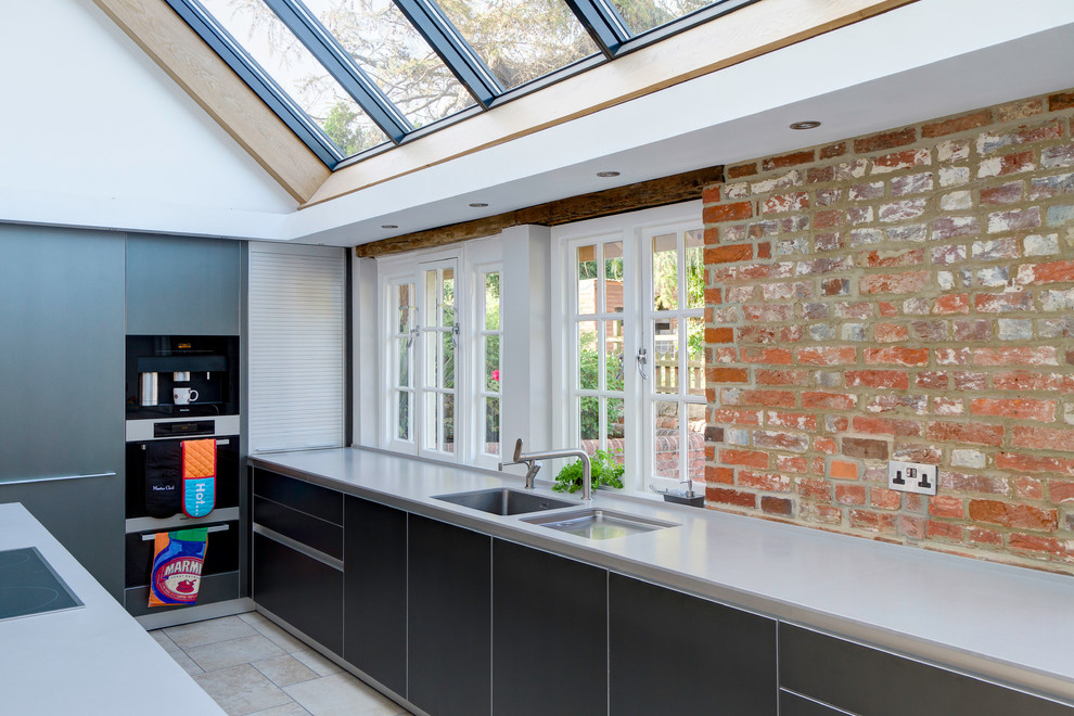Zweizeilige Moderne Wohnküche mit flächenbündigen Schrankfronten, grauen Schränken, Quarzwerkstein-Arbeitsplatte, schwarzen Elektrogeräten und Kücheninsel in Wiltshire