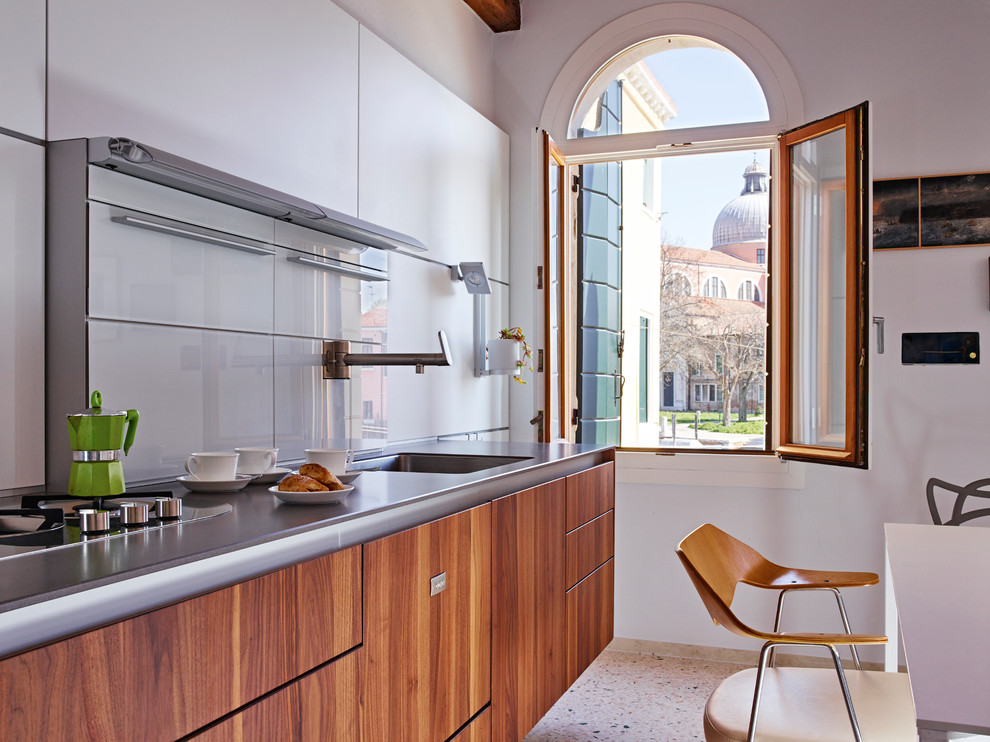 Eat-in kitchen - mid-sized contemporary eat-in kitchen idea in Venice with a drop-in sink, flat-panel cabinets, medium tone wood cabinets, solid surface countertops, white backsplash, glass sheet backsplash, paneled appliances and no island