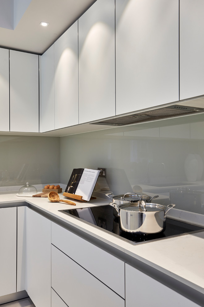 Geräumige Moderne Wohnküche in L-Form mit integriertem Waschbecken, flächenbündigen Schrankfronten, weißen Schränken, Quarzwerkstein-Arbeitsplatte, Küchenrückwand in Beige, Glasrückwand, schwarzen Elektrogeräten und Kücheninsel in London