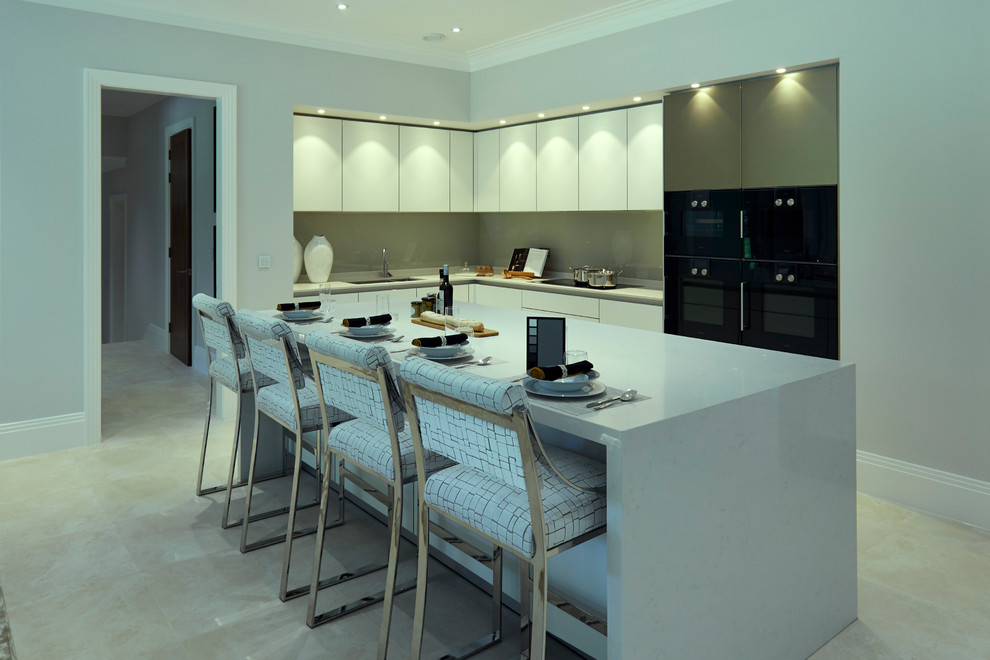 This is an example of an expansive contemporary l-shaped kitchen/diner in London with an integrated sink, flat-panel cabinets, white cabinets, engineered stone countertops, beige splashback, glass sheet splashback, black appliances and an island.