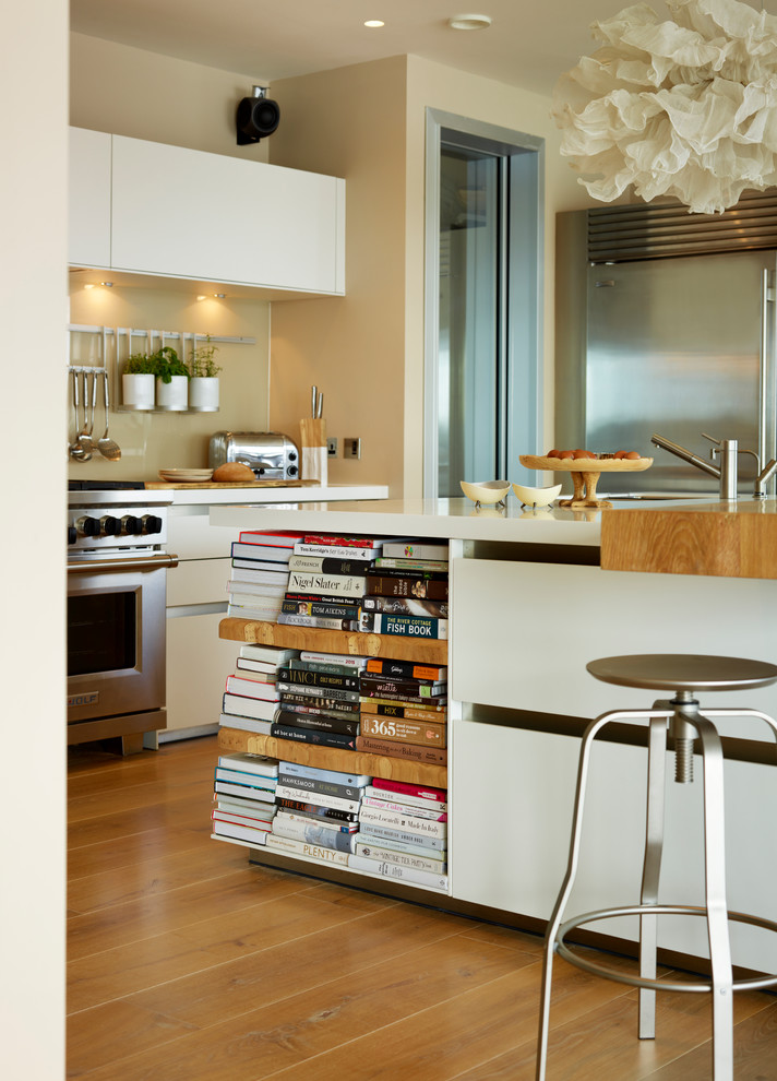 Offene, Große Moderne Küche in L-Form mit flächenbündigen Schrankfronten, Glasrückwand, Küchengeräten aus Edelstahl, braunem Holzboden und Kücheninsel in Wiltshire