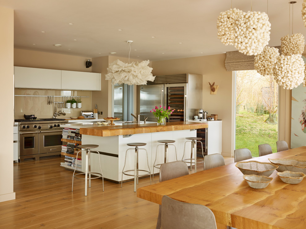 Offene, Große Moderne Küche in L-Form mit flächenbündigen Schrankfronten, Glasrückwand, Küchengeräten aus Edelstahl, braunem Holzboden und Kücheninsel in Wiltshire