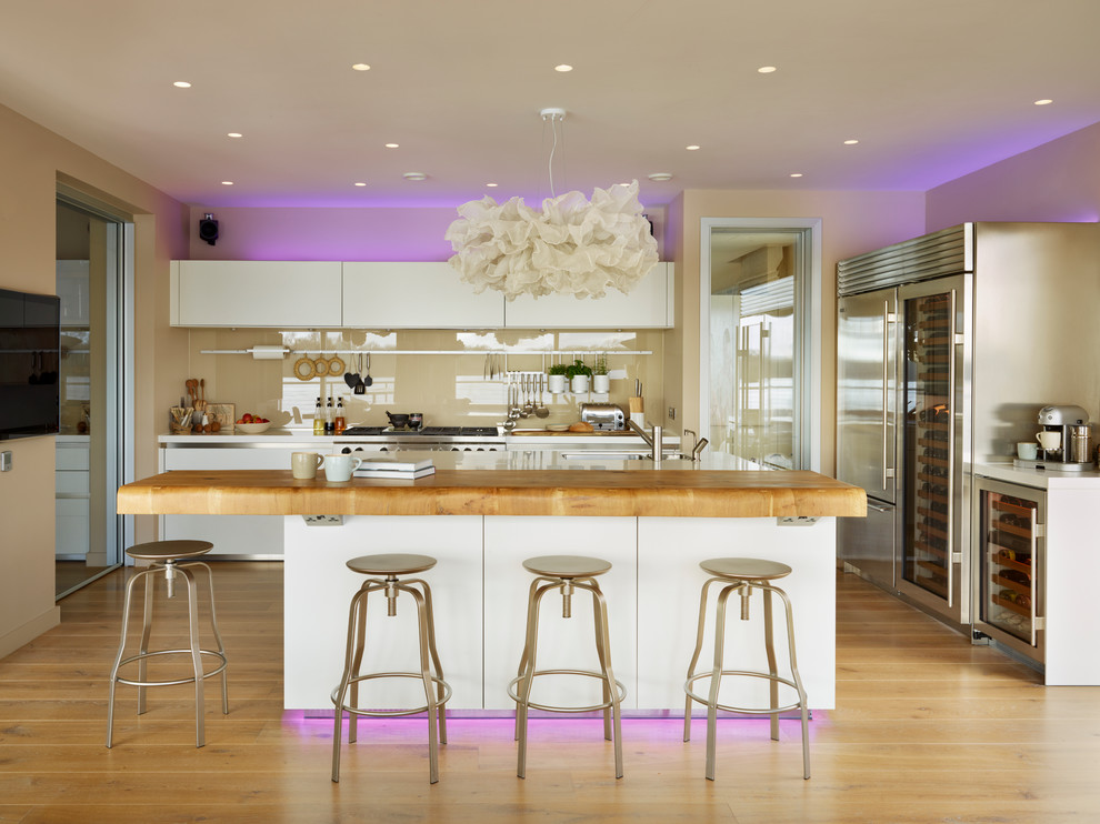 Foto på ett stort funkis kök, med släta luckor, glaspanel som stänkskydd, rostfria vitvaror, mellanmörkt trägolv, en köksö och en undermonterad diskho