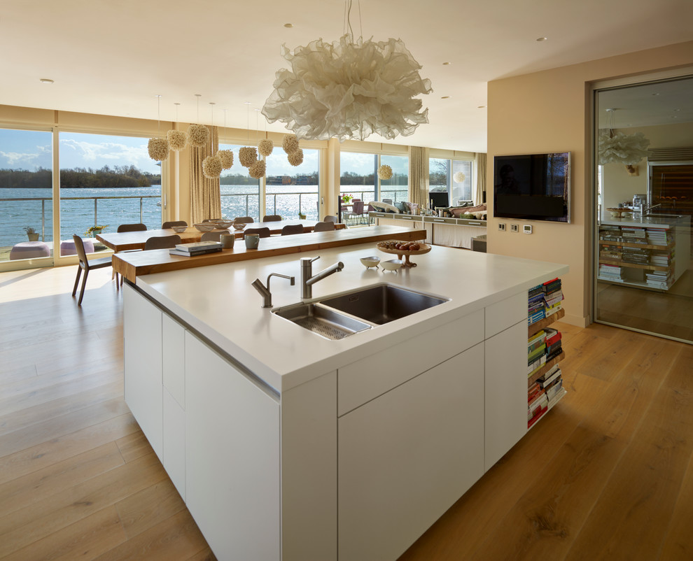 Large trendy l-shaped medium tone wood floor open concept kitchen photo in Wiltshire with flat-panel cabinets, glass sheet backsplash, stainless steel appliances, an island and an undermount sink
