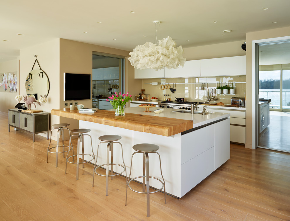 Immagine di una grande cucina design con ante lisce, ante bianche, paraspruzzi con lastra di vetro, elettrodomestici in acciaio inossidabile, pavimento in legno massello medio e lavello sottopiano
