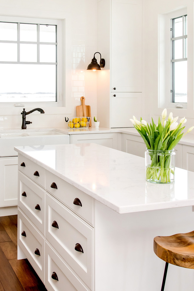 Exempel på ett lantligt kök, med en rustik diskho, luckor med infälld panel, vita skåp, granitbänkskiva, vitt stänkskydd, rostfria vitvaror, mellanmörkt trägolv, en köksö och brunt golv
