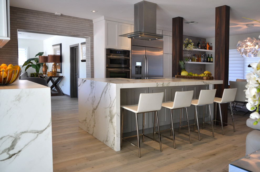 Open concept kitchen - mid-sized coastal l-shaped porcelain tile open concept kitchen idea in Miami with a farmhouse sink, shaker cabinets, white cabinets, quartz countertops, gray backsplash, porcelain backsplash, stainless steel appliances and an island