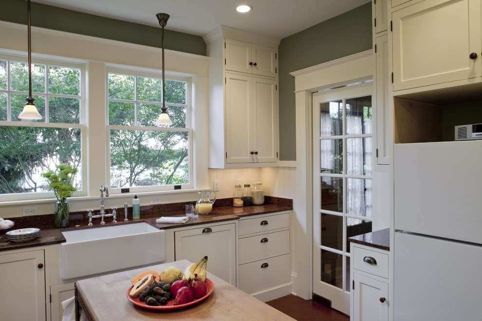 Example of a mid-sized arts and crafts l-shaped linoleum floor enclosed kitchen design in Portland with a farmhouse sink, shaker cabinets, white cabinets, granite countertops, white backsplash, ceramic backsplash, white appliances and an island