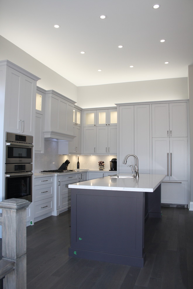 Ejemplo de cocina contemporánea, grande, con fregadero de doble seno, armarios estilo shaker, puertas de armario grises, encimera de cuarzo compacto, salpicadero verde, electrodomésticos de acero inoxidable, suelo de madera en tonos medios, una isla, suelo marrón y encimeras grises
