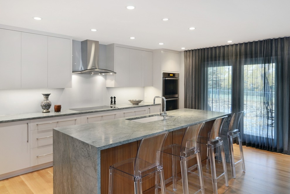 Inspiration for a contemporary kitchen in Calgary with a submerged sink, flat-panel cabinets, white cabinets, granite worktops, grey splashback, stainless steel appliances, light hardwood flooring and an island.