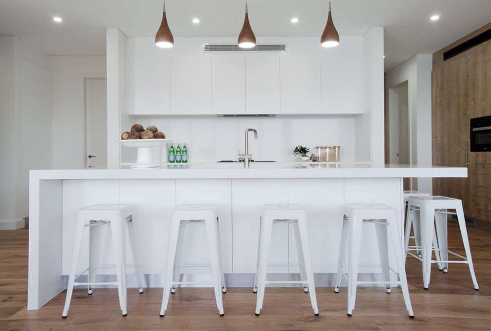 Immagine di un cucina con isola centrale minimal con ante lisce, ante bianche, paraspruzzi bianco e pavimento in legno massello medio