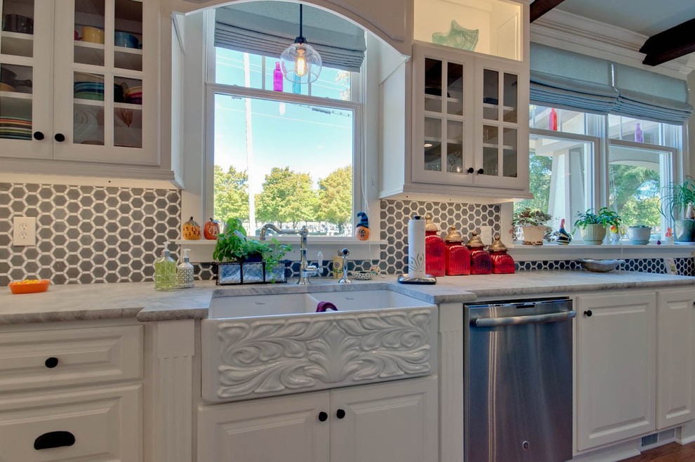 Mid-sized arts and crafts u-shaped light wood floor enclosed kitchen photo in Other with a farmhouse sink, raised-panel cabinets, white cabinets, marble countertops, gray backsplash, ceramic backsplash, stainless steel appliances and an island