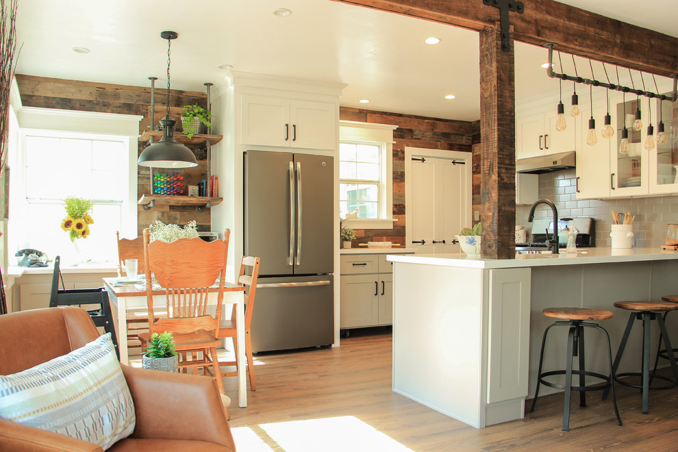 Small country u-shaped laminate floor and brown floor eat-in kitchen photo with a farmhouse sink, shaker cabinets, gray cabinets, quartz countertops, gray backsplash, subway tile backsplash and a peninsula