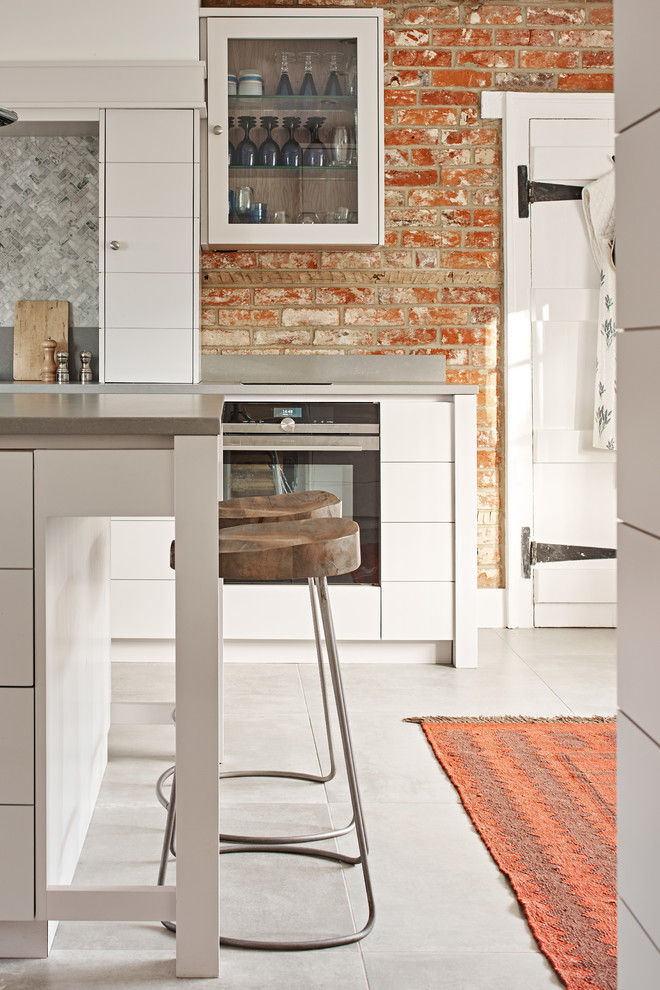 Design ideas for an urban kitchen in Berkshire with flat-panel cabinets, white cabinets, red splashback, stainless steel appliances and an island.