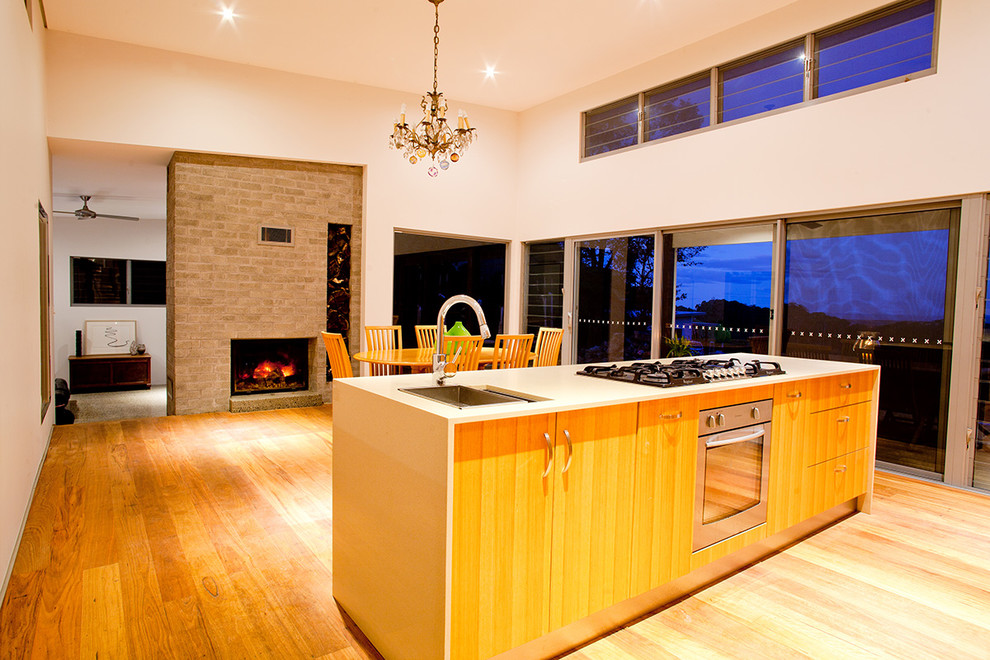 Imagen de cocina comedor actual de tamaño medio con puertas de armario de madera clara, electrodomésticos de acero inoxidable, suelo de madera clara y una isla