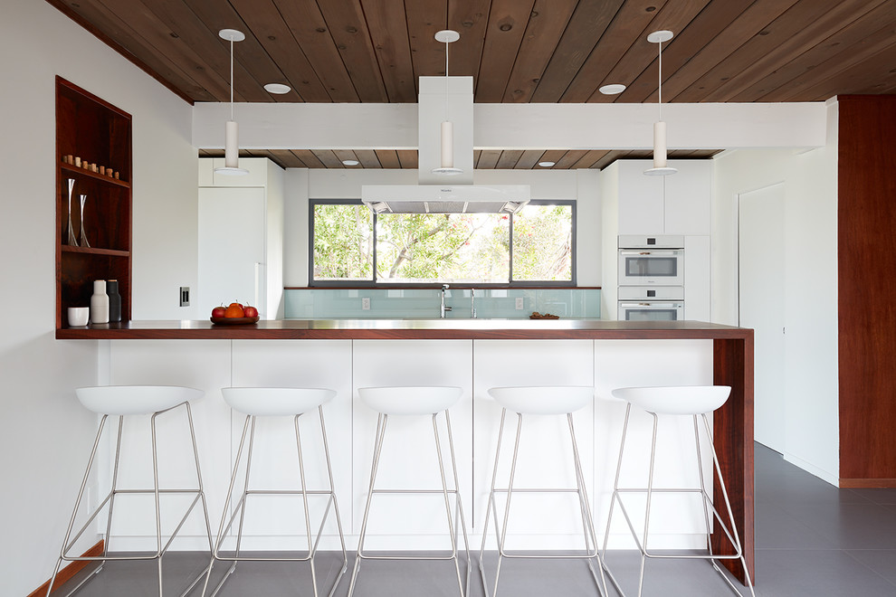 Foto di una cucina moderna con paraspruzzi blu, paraspruzzi con lastra di vetro, elettrodomestici bianchi, penisola e pavimento grigio
