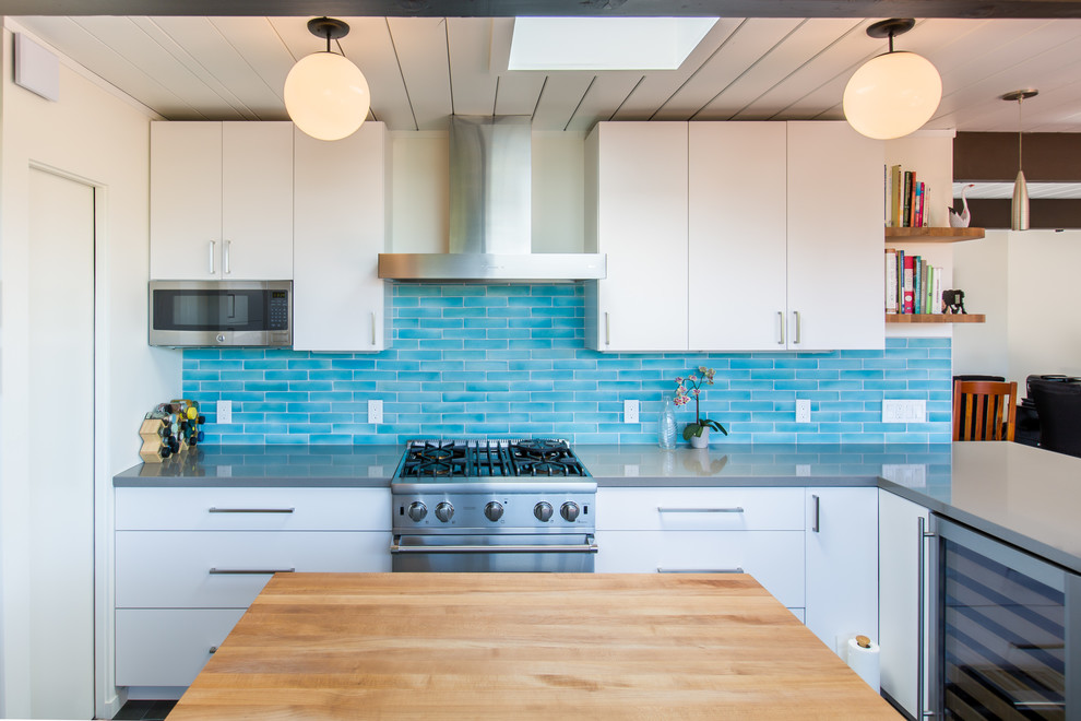 This is an example of a midcentury kitchen in San Francisco with flat-panel cabinets, white cabinets, engineered stone countertops, blue splashback, glass tiled splashback and stainless steel appliances.