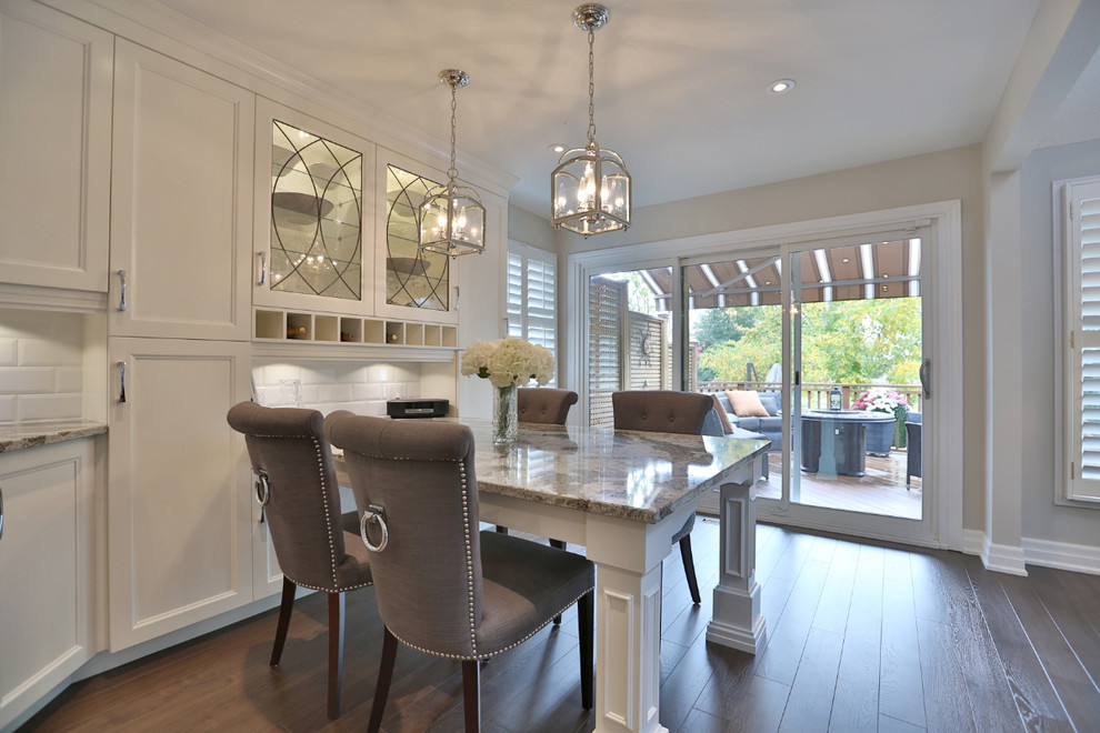 This is an example of a large traditional u-shaped kitchen/diner in Toronto with shaker cabinets, white cabinets, engineered stone countertops, white splashback, metro tiled splashback, stainless steel appliances, medium hardwood flooring and no island.