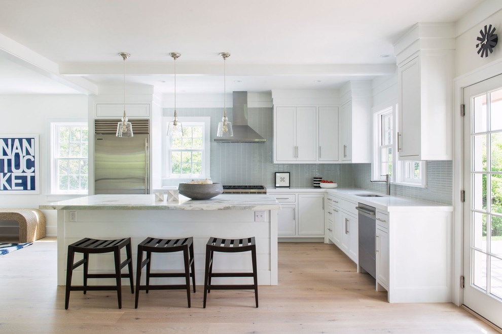 Example of a large trendy l-shaped light wood floor kitchen design in Providence with an undermount sink, shaker cabinets, white cabinets, marble countertops, gray backsplash, glass tile backsplash, stainless steel appliances and an island