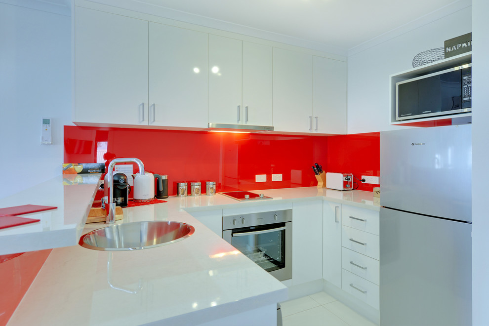 Esempio di una piccola cucina minimalista con lavello da incasso, ante bianche, top in laminato, paraspruzzi rosso, paraspruzzi con lastra di vetro, elettrodomestici in acciaio inossidabile, pavimento con piastrelle in ceramica e penisola