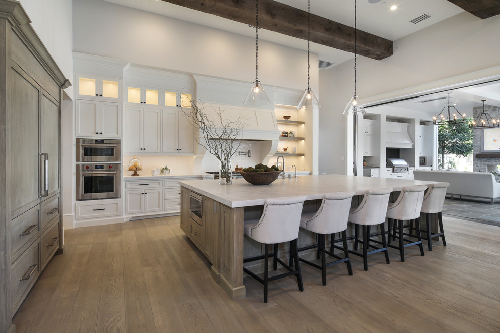 Photo of a traditional l-shaped kitchen in Orange County with shaker cabinets, white cabinets, stainless steel appliances, medium hardwood flooring, an island, brown floors and white worktops.