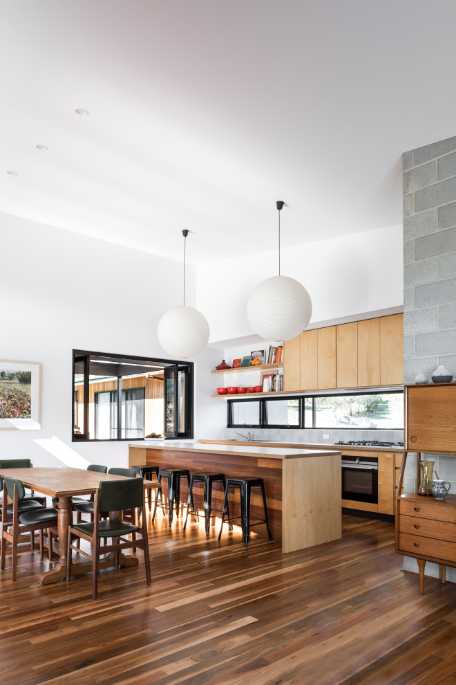 Idée de décoration pour une cuisine ouverte parallèle design en bois brun avec un placard à porte plane, un électroménager noir, parquet foncé, îlot et un sol marron.