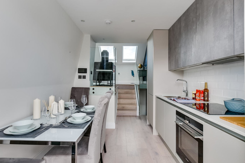 Small contemporary single-wall open plan kitchen in London with a single-bowl sink, flat-panel cabinets, grey cabinets, quartz worktops, white splashback, glass tiled splashback, black appliances, laminate floors, no island and grey floors.